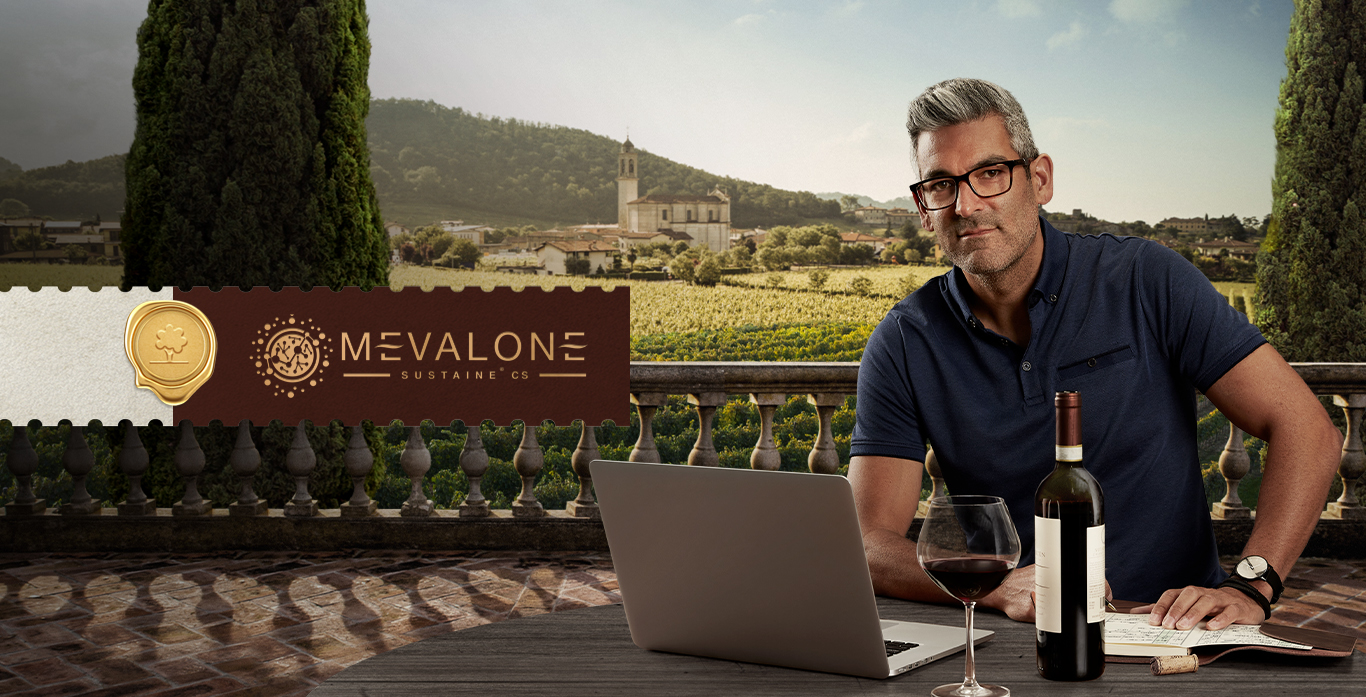 Man sitting with a laptop and glass of wine in front of him.